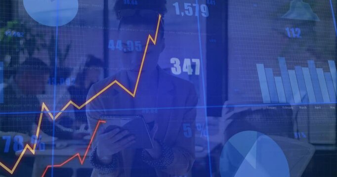 Professional woman holding tablet showing finance graphs in office while colleagues reviewing data