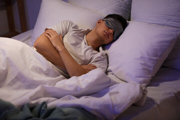 Handsome young man with mask sleeping on bed in evening at home