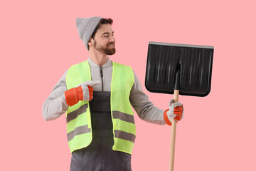 Male scavenger pointing at snow shovel on pink background