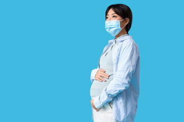 Pregnant Asian woman in medical mask on blue background