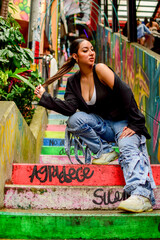Confident Latina woman posing on colorful graffiti stairs in Medellín