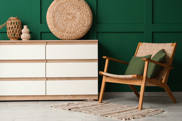 Interior of stylish living room with cozy wooden armchair, chest of drawers and wicker pouf