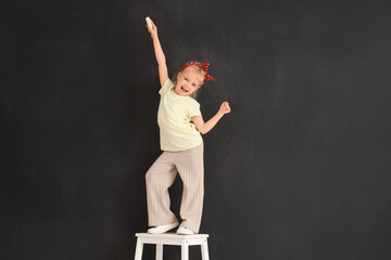 Cute little girl with chalk piece on stool near black wall