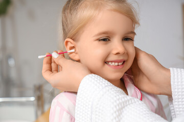 Mother with cotton bud cleaning her little daughter's ears in bathroom, closeup