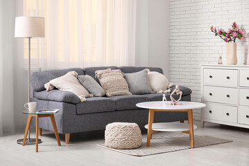 Cozy sofa, armchair and chest of drawers with blooming magnolia branches in interior of living room