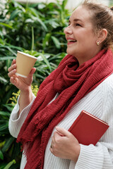 Smiling mature woman drinking coffee and holding a book in a botanical garden