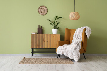 Brown armchair and chest of drawers near green wall in interior of room
