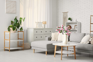 Comfortable sofa and blooming magnolia branches in vase on coffee table in interior of living room