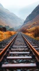 Fototapeta premium Railway tracks leading into a valley, with mountains and a cloudy sky in the background