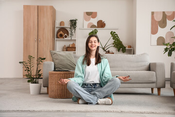 Happy young woman meditating on floor in living room