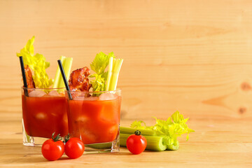 Glasses of bloody mary cocktail with bacon and celery on wooden background
