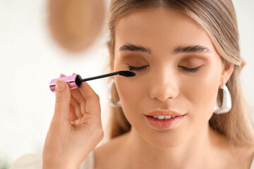 Professional makeup artist applying mascara on young woman in studio, closeup