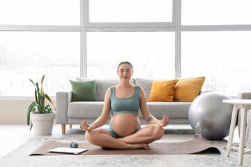 Sporty pregnant woman meditating on mat at home
