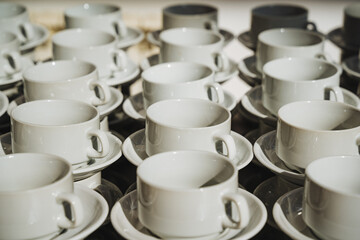 On a beautifully arranged table, there is a charming row of pristine white coffee cups and accompanying saucers, creating an inviting atmosphere for enjoying delicious beverages