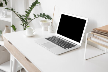 Blank laptop with coffee cup and plant on desk in home office