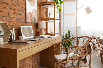 Workplace with laptop and books near brick wall in home office