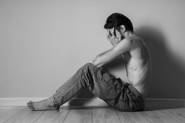 Young man with anorexia sitting near wall