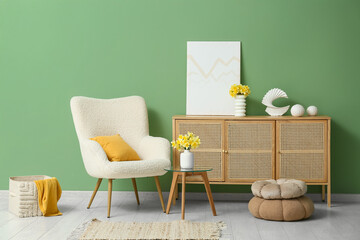 Cozy armchair with dresser, coffee table and narcissus flowers near green wall in living room