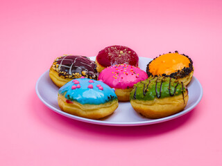 Colorful assorted donuts with vibrant icing and toppings on a white plate over a pink background