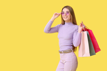 Pretty young woman in sunglasses with shopping bags on yellow background