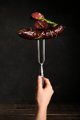 Hand holding meat fork with tasty blood sausage on dark background