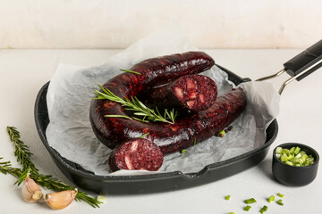 Frying pan with tasty blood sausage on light background