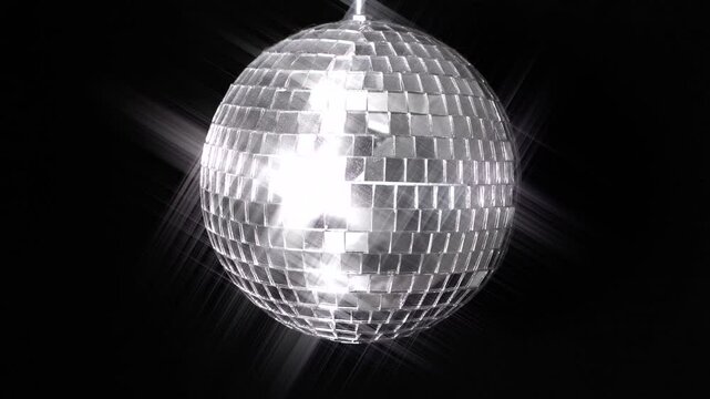 A rotating mirror ball, or disco ball, spinning against black. Background light decoration for a dance club nightclub music party room. A star filter added for a pleasing shine and reflective effect.