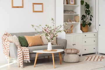 Interior of light living room with flowering branches in vase, closet and sofa