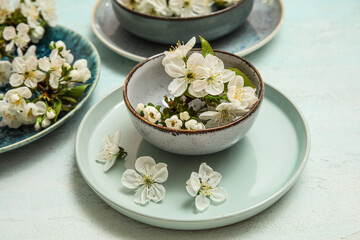 Different clean plates with blooming branches on light blue background, closeup