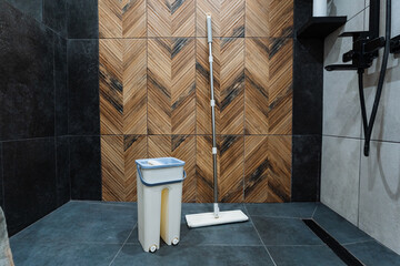 A clean bathroom features a mop and trash can neatly placed on the floor, with a warm wooden wall that adds character, creating a cozy atmosphere for relaxation or refreshment