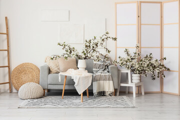 Interior of light living room with sofa and flowering branches in vases