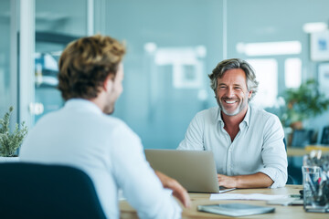 Obraz premium Two businessmen smiling and collaborating on a project while working on a laptop in a modern office environment, fostering teamwork and innovation