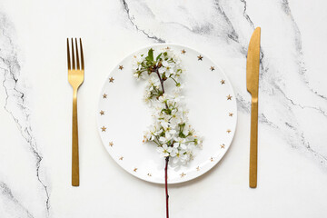 Beautiful table setting with golden cutlery and blooming branch on white background