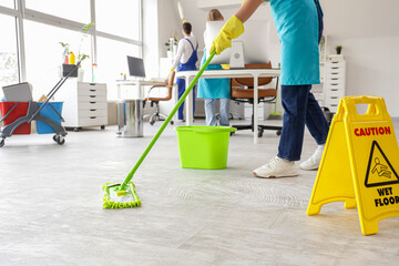 Female janitor mopping floor and her team cleaning in office