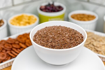 Close-up white bowl with healthy flax seeds on blurred background of cups with cereals