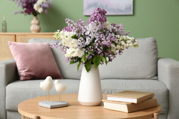 Vase with lilac flowers, decor and books on table in living room