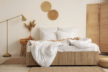 Interior of cozy room with soft linen on bed, table and lamp