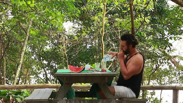 Man on picnic in park. Making and drinking watermelon juice.