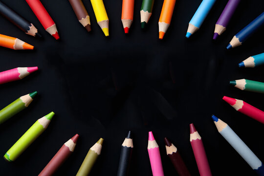 Colored pencils arranged in a circle on black