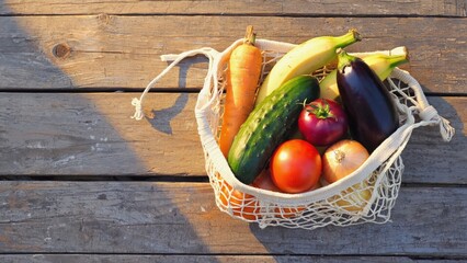 Vegetables and fruits in net bag on wooden planks, sunlit, simple