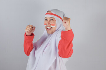 Smiling Indonesian woman in red and white hijab costume raising fists in enthusiastic pose with...