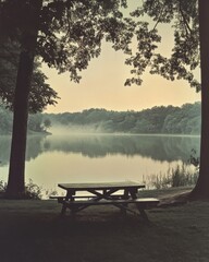 Obraz premium Tranquil lake scene with picnic table in foreground at dawn misty water reflection scenic
