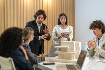 Architects engineers collaborating on building design project in modern office, diverse team of professionals female muslim architect and male engineers discussing architectural model of structure