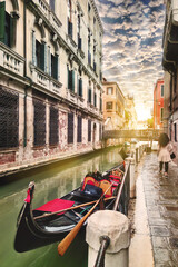 A traditional gondola rests on a serene Venice canal during golden hour, ancient buildings bathed in warm sunset light, capturing the city's timeless romantic charm