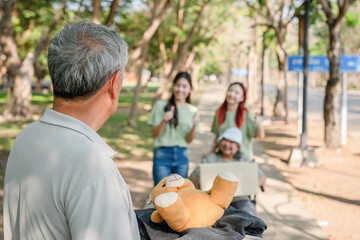 Senior man donating toys in park, Group of Happy Asian volunteers team in park for charity event.