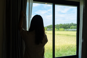 The housekeeper is arranging the curtains and cleaning the windows of the resort bedroom