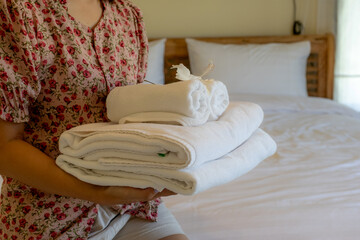 Hands of hotel maid putting plumeria flower and towels on the bed in the luxury hotel room ready for tourist travel