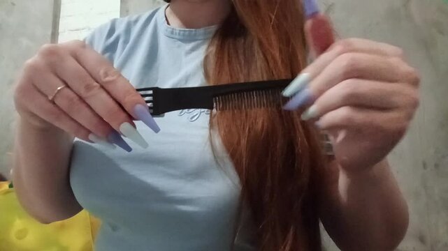 Female hands with long nails scrape a comb, then the woman combs her hair