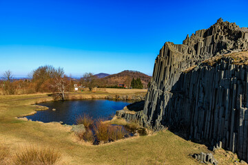 Majestic basalt rock formations by tranquil pond under clear blue sky