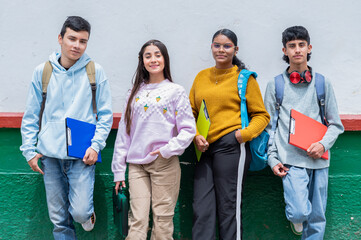 Latino high school students standing against wall with notebooks and backpacks